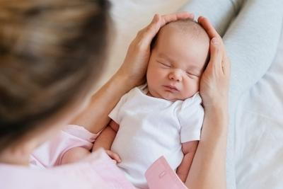 Mother taking care her baby by holding head on bed