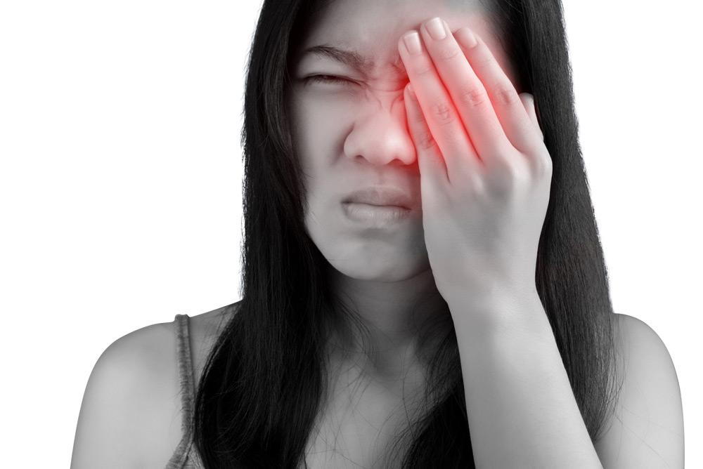 A woman covering her left eye in pain