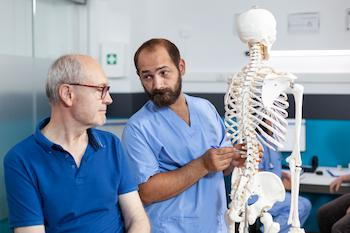 Chiropractor showing spinal cord bones to aged man
