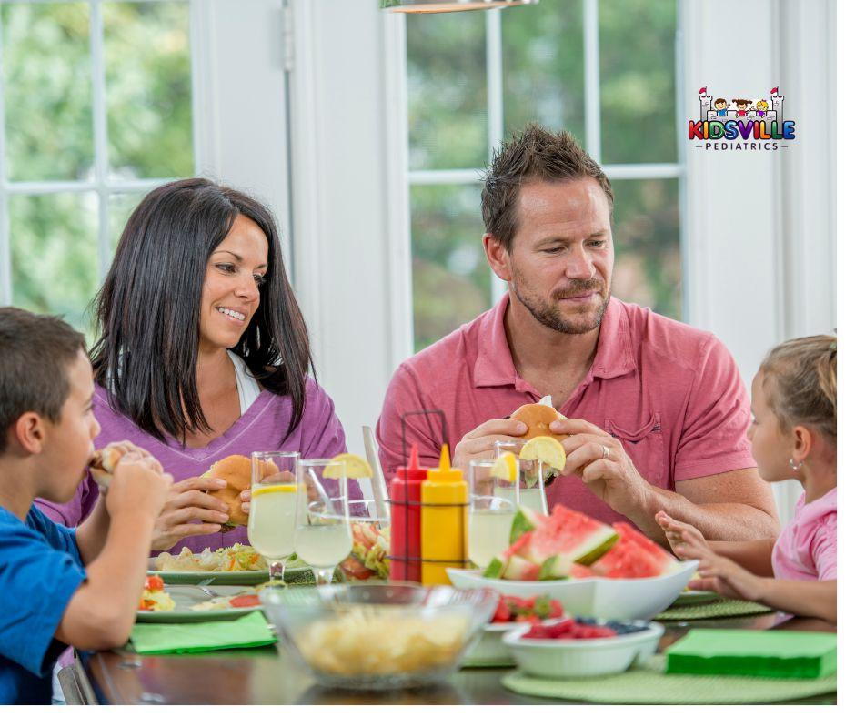 alt=A family enjoying a meal at the table, with watermelon and sandwiches.