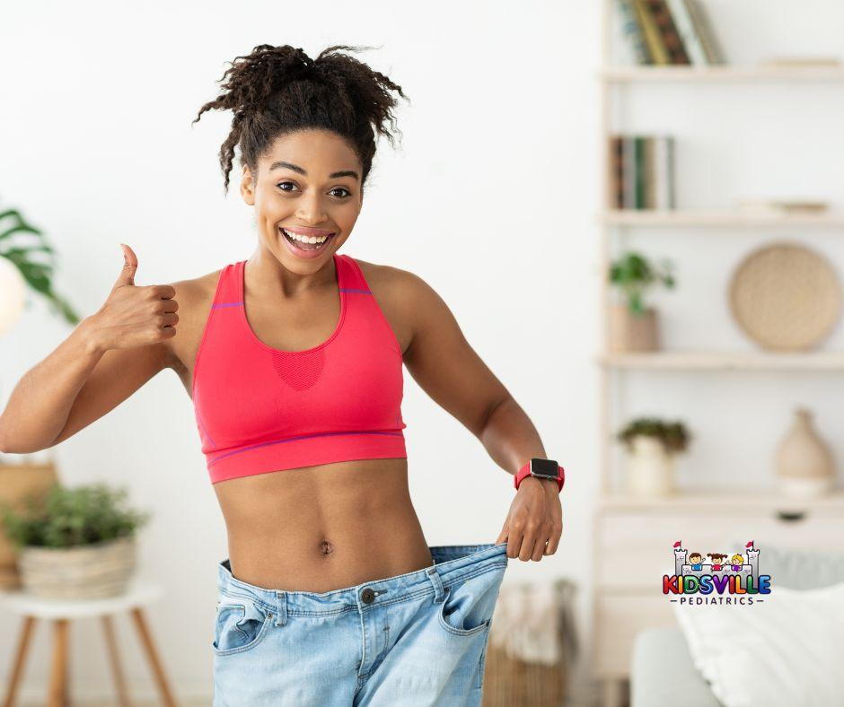 Woman in red sports bra holding up jeans and showing weight loss.