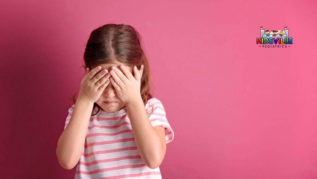 A young girl peeking through her fingers, covering her eyes with her hands.