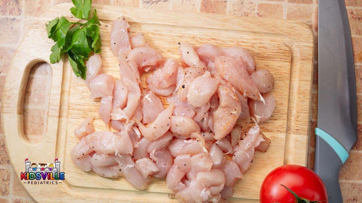 A cutting board with raw chicken and tomatoes.