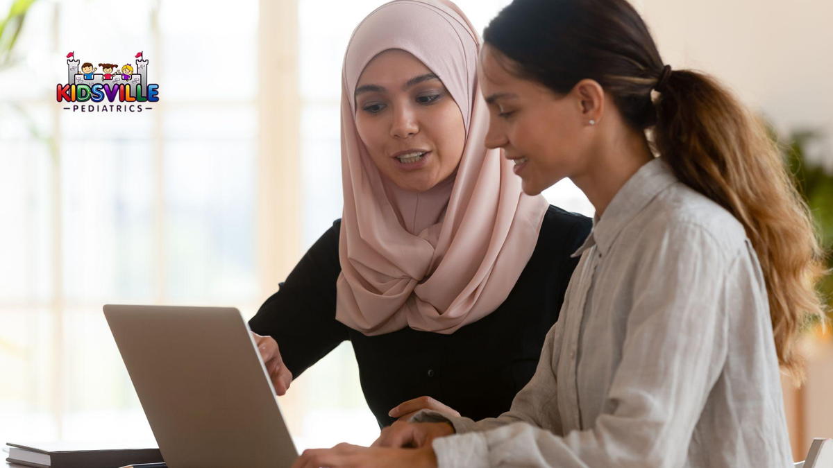 Two women, one wearing hijab, engaged in conversation at a table, with a laptop open between them, sharing ideas and collaborating.