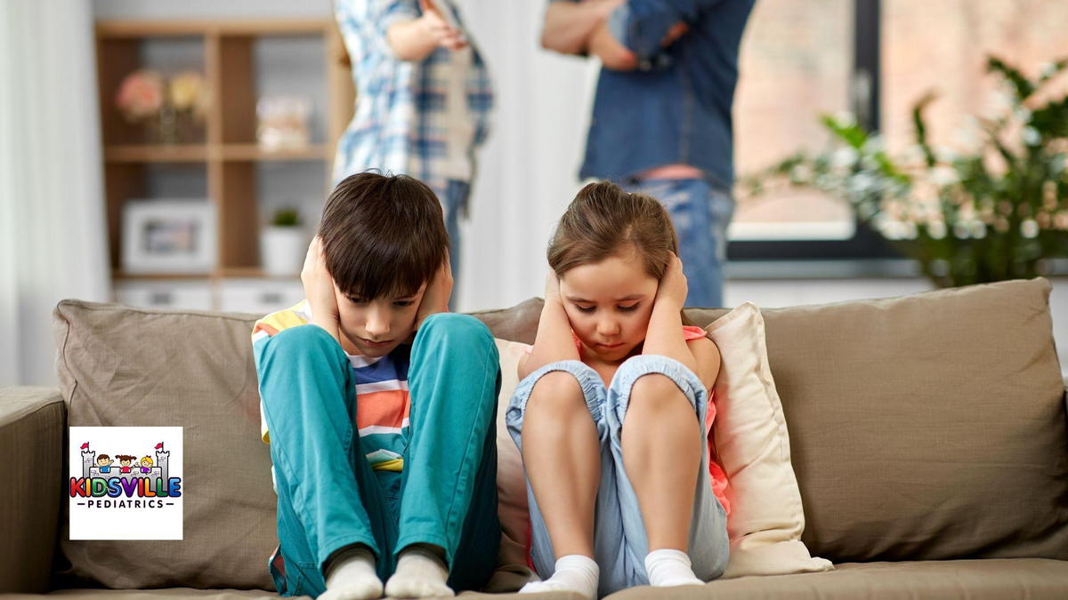 Two children sit on a couch, their heads resting in their hands as their parents quarrel in the background.