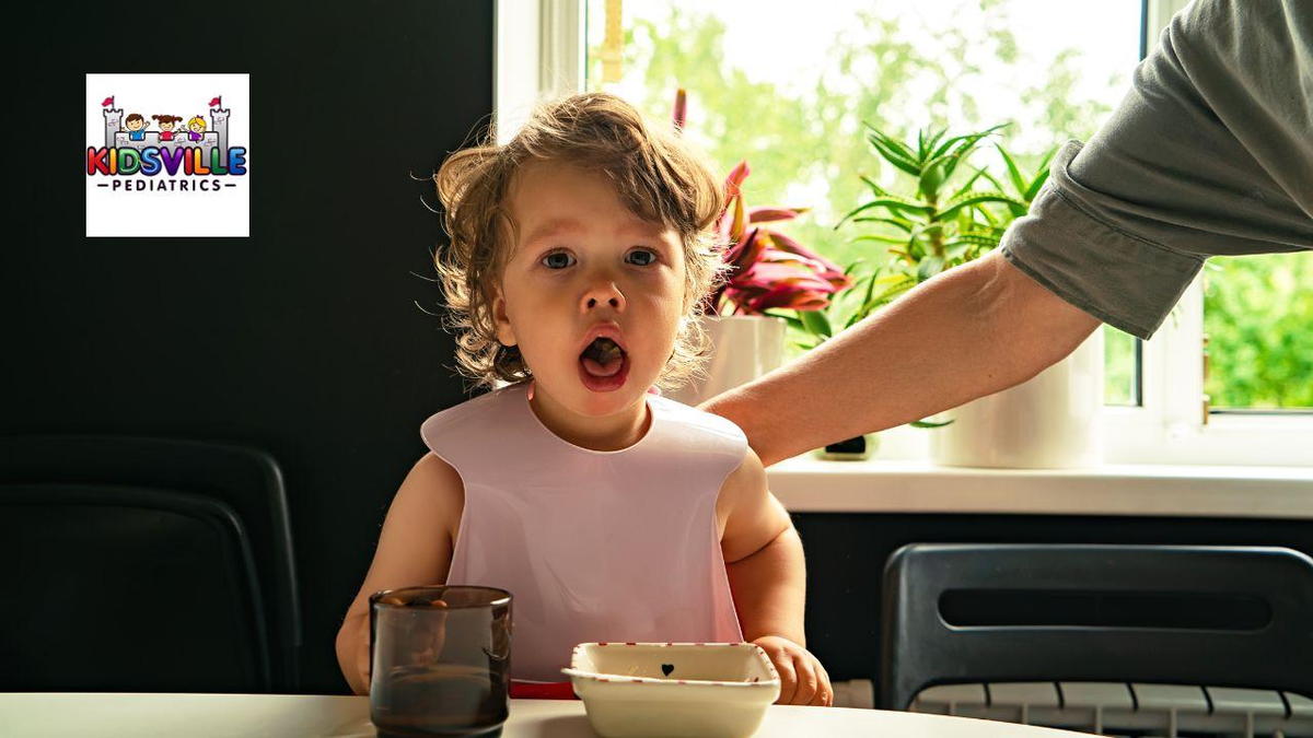 A child sits at a table, choking on a bowl of food and being helped by an adult.