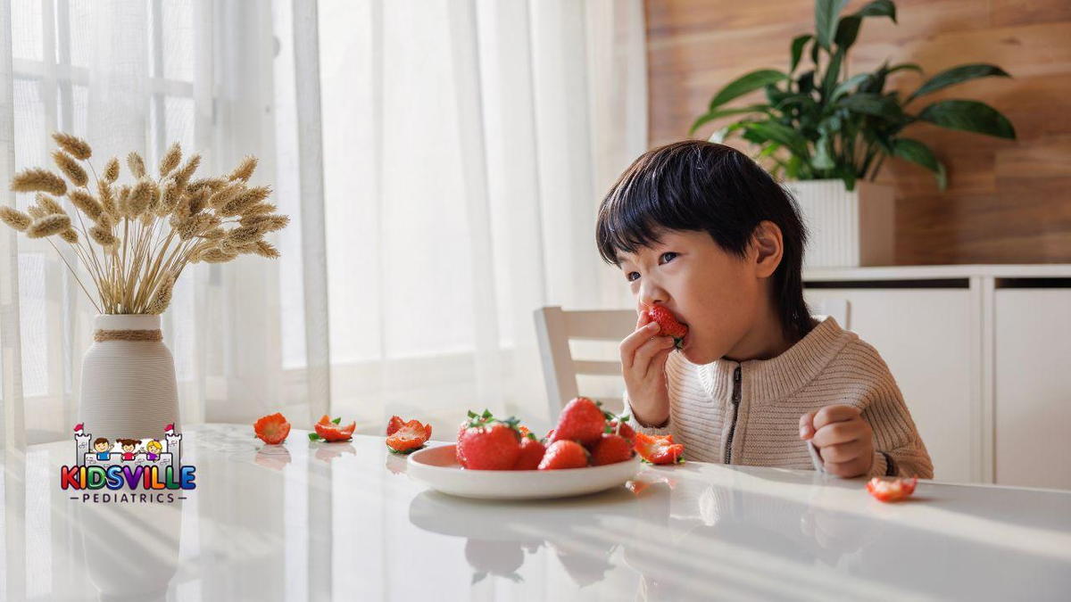 A young boy happily eating fresh strawberries while sitting at a table, enjoying a delightful snack.