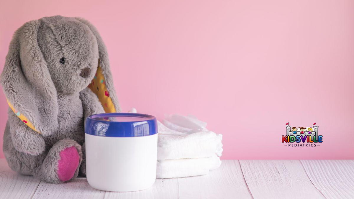 A stuffed rabbit beside a stack of diapers and a jar of cream.