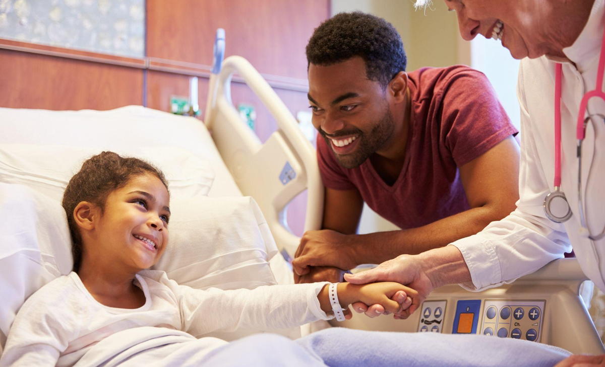 A doctor gently examines a young girl lying in a hospital bed, providing care and comfort during her treatment.