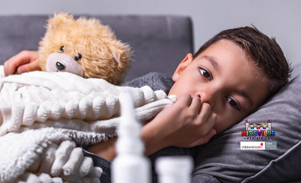 A child cuddles a stuffed animal while wrapped in a cozy blanket, seemingly ill.