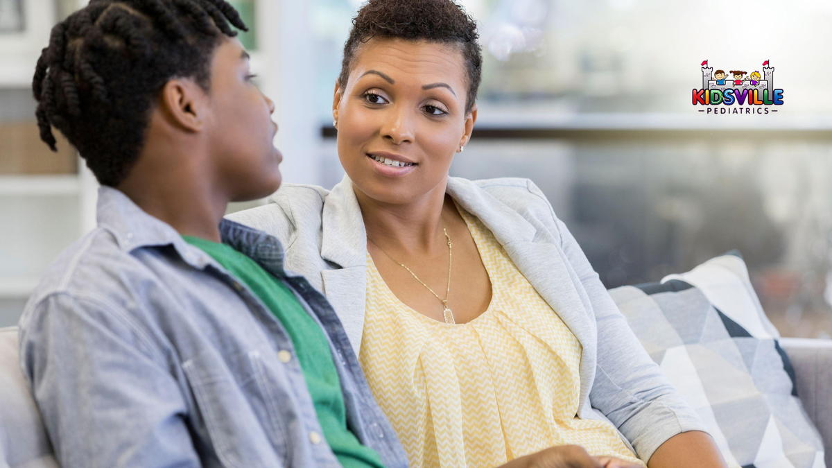 A woman talking with her teenage son while they are seated in a couch.