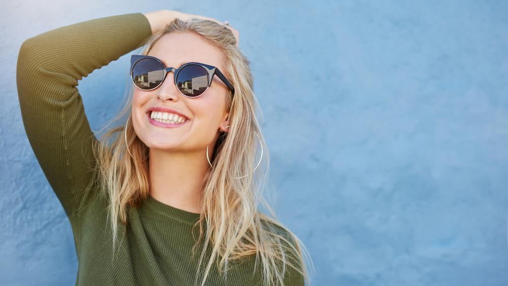woman in sunglasses smiling holding her hair