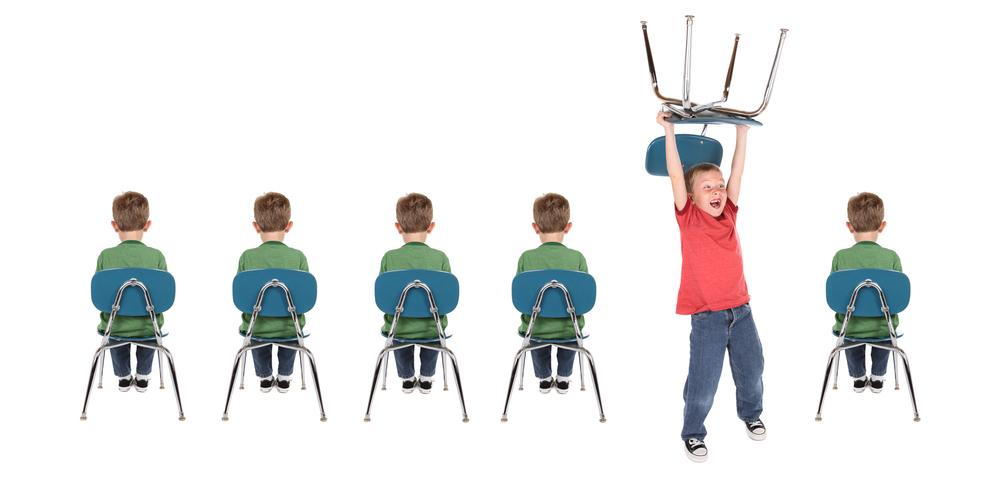 Child holding chair above head while other children are sitting still