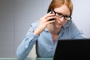 A young female business manager behind a computer talks on a mobile phone.