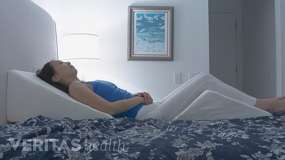 Image of young woman sleeping with a wedge pillow underneath her back and legs.